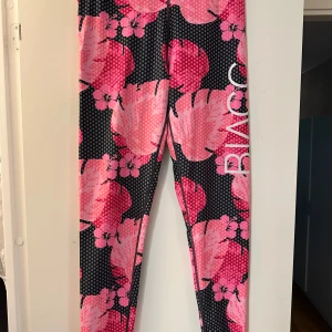 Blommiga trännings leggings från Blacc strl: L - Snygga leggings från Blacc med stort blommönster i rosa och svart. De har en tajt passform och är perfekta för träning. Materialet är stretchigt syntet som sitter skönt mot kroppen. Stora vita bokstäver längs benet ger en sportig vibe. Lös tråd mellan låren men ingenting som är hål eller så.