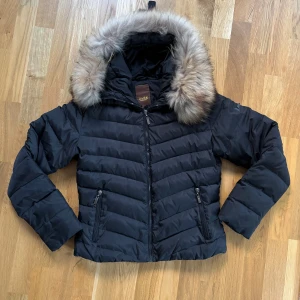Svart dunjacka Bark of Sweden pälskrage strl 38 - Svart dunjacka Bark of Sweden m pälskrage strl 38. Liten lagning vid dragkedjan (se sista bild). Midjelång modell. Jag är strl S vanligtvis och mig passar den bra både utan och med tjocktröja under.