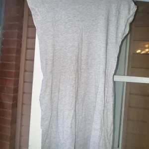 Grå basic klänning 146/152 - Enkel och mjuk grå långklänning från H&M Basic. Klänningen har rund halsringning och är ärmlös, tillverkad i bomullsmix som känns skön mot huden. Passform: avslappnad. Defekt: se bild 3.