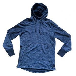 Fleece Hoodie - Snygg mörkgrå hoodie från Under Armour med huva och snörning. Tröjan har långa ärmar, ribbade muddar och praktiska fickor framtill. Sidosömmen har dragkedja för extra stilpoäng och bekvämlighet. Perfekt för chill eller träning.