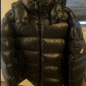 Moncler Maya Giubbotto Jacket  - Säljer en helt ny svart pufferjacka från Moncler med klassisk logga på ärmen och avtagbar huva. Jackan har dragkedja framtill, stora fickor och quiltad design. Insidan har Monclers ikoniska serietidningsetikett. Perfekt för kalla dagar och riktigt snygg streetstil. storlek (7).          - kan gå ner i pris vid snabb affär  - Finns i Göteborg  - Kan även fraktas