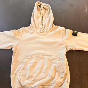 Beige hoodie från Stone Island - Säljer en beige hoodie från Stone Island med klassisk patch på ärmen. Tröjan har känguruficka framtill, huva och långa ärmar. Tillverkad i mjuk bomull, perfekt för chill dagar. Enkel och stilren design som funkar till det mesta.