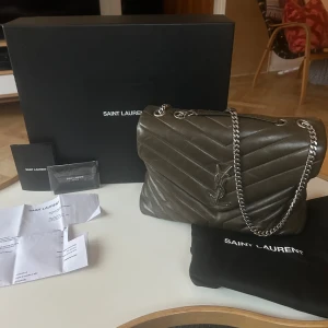 Saint Laurent quiltad axelväska i skinn - Säljer nu min Saint Laurent Loulou väska i medium och färgen khaki med originaldetaljer såsom box, dustbag etc (se allt som inkluderas på bilden). Väskan säljs inte längre ny, men såldes för cirka 27 000kr då den såldes ny. Den är i bra allmänt skick med generella defekter såsom veck, hörnslitage, repor, lätt missfärgning av kedjan etc som visas på bilderna. Måtten är 32 x 22 x 12 cm. Skriv för fler bilder på väskan. Tryck ej på köp nu utan att ha skrivit till mig först! Pris kan diskuteras❤️