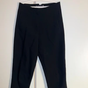 Svarta kostymbyxor från Amisu - Svarta kostymbyxor från Amisu i klassisk rak modell. Byxorna har hög midja, diskreta fickor framtill och är sydda i ett mjukt tyg som ger en stilren look. Perfekta för dig som gillar en clean och enkel stil.