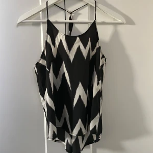 Svartvitt linne med zigzag-mönster - Söt ärmlös linnetopp med svartvitt zigzag-mönster och tunna axelband. Toppen har lös passform och ett band i ryggen som knyts. 