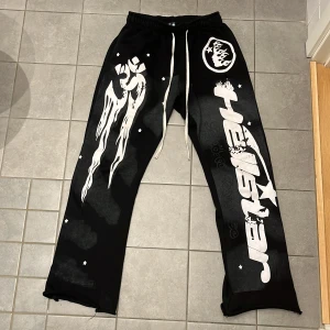 Svarta Hellstar mjukisbyxor med tryck - Svarta mjukisbyxor från Hellstar med feta vita tryck och grafik längs benen, elastisk midja med vit snörning och raka ben. Snygga detaljer med stjärnor och logga, perfekt för en streetwear-look. 