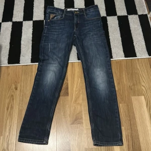Blå jeans från Detroit Stylingex - Säljer ett par klassiska blå jeans från Detroit Stylingex i storlek 152. Jeansen har raka ben, snygga slitningar och kontrastsömmar. De har fem fickor och detaljerade bakfickor med dragkedjor. Perfekta för en avslappnad och cool look.
