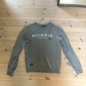 Grå stickad tröja från Morris Rowing Club - Snygg grå stickad tröja från Morris Rowing Club med vit text och klubbmärke framtill. Tröjan har ribbade muddar vid ärmslut och nederkant samt rund hals. Perfekt för dig som gillar klassisk och stilren stil inga fel på den skriv vid frågor 
