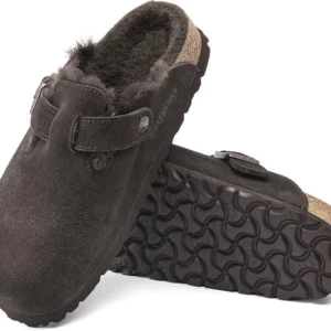 Birkenstock Boston Shearling 39 - Mörkbruna sandaler från Birkenstock i mjuk mocka med pälsfoder. Skorna har en bred rem med spänne och platt sula, perfekt för att hålla fötterna varma. Klassisk rund tå och bekväm slip-in modell. Använda fåtal ggr. 