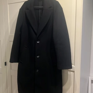 Svart klassisk kappa med knappar från bershka - Svart kappa med stilren design och tre knappar framtill. Jackan har bred krage, två stora fickor och är helsvart utan mönster. Kappan är från bershka och är i extremt bra skikt och har jätte bra kvalitet som håller dig varm under både vintern och hösten.