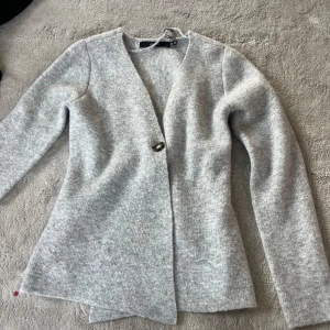 Ljusgrå kofta från H&M med knapp - Grå stickad figursyddtröja. Väldigt mjuk och inte alls sticksig. Lite längre i modellen 