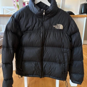 The North Face pufferjacka svart - Svart pufferjacka från The North Face i storlek M. Jackan har hög krage, dragkedja framtill och två fickor. Klassisk logga broderad på bröstet. Säljer för 600 kr. Finns i Kalmar, kan skickas mot fraktkostnad. 