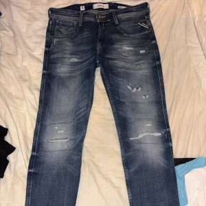 Replay blå slitna jeans, midja 30/32 - Säljer ett par helt nya blå jeans från Replay med snygga slitningar och tvättade detaljer. Klassisk femficksmodell med raka ben och normal passform. Jeansen har Replay-logga på bakfickan och patch i läder bak i midjan. 