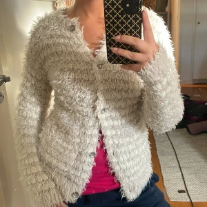 Fluffig vit kofta med knappar - Supermysig fluffig vit kofta med knappar framtill. Koftan är stickad med ett lurvigt garn som ger en cool textur och har långa ärmar. Perfekt för lager-på-lager och att mysa i under kyliga dagar.