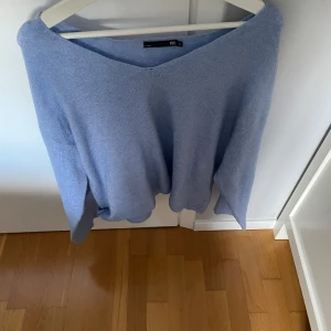 Ljusblå stickad tröja från 157 - Mysig ljusblå stickad tröja från 157 med v-ringad hals och avslappnad passform. Perfekt för lager-på-lager och chill dagar. Långa ärmar och mjukt material gör den superbekväm.