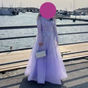 Ljuslila långklänning med pärlor - Magisk ljuslila långklänning med glittriga pärldetaljer över hela klänningen. Klänningen har långärmade meshärmar och en vid, svepande kjol. Perfekt för bal eller speciella tillfällen när du vill sticka ut och känna dig som en prinsessa. Nypris 4000kr, använt endast på min bal. 