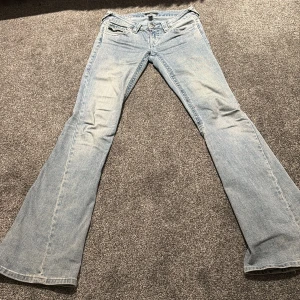 True Religion Joey flare jeans ljusblå - Säljer ett par ikoniska True Religion Joey jeans i ljusblå tvätt med låg midja och flare-ben. Klassiska detaljer med stora ficklock bak och snygga kontrastsömmar. Perfekta för dig som gillar en retro vibe och vill sticka ut med coola jeans.