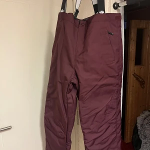 Vinröda täckbyxor från Ski Industries XL - Säljer ett par vinröda täckbyxor från Ski Industries i storlek XL. Byxorna har hängslen, dragkedja och knapp framtill samt en ficka med dragkedja. Materialet är vind- och vattenavvisande, perfekt för kalla dagar i backen.