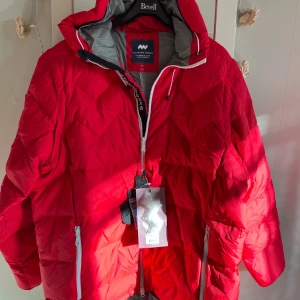 Mountain Works röd parka, storlek XXL - Riktigt fet röd dunjacka från Mountain Works, Sport Hybrid Collection. Jackan har huva, vita dragkedjor, quiltad design och coolt brittiskt flaggmärke på ärmen. Fylld med dun och fjädrar för max värme. Perfekt för kalla dagar och har en loose passform. Armarna är avtagbara 