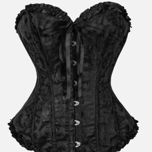 Svart korsett med rosett och mönster - Säljer en svart korsett med snyggt blommigt mönster, söt rosett framtill och dekorativa knappar. Toppen har en markerad midja och volangkant upptill och nedtill för extra detalj. Perfekt för dig som vill sticka ut med en edgy och trendig look.