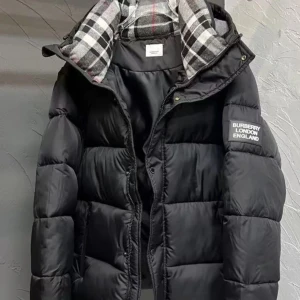 Burberry jacka/ väst - Säljer en svart pufferjacka från Burberry med klassisk logotyp på ärmen. Jackan har en huva med rutigt foder i grått, vitt och rött, samt dragkedja och knappar framtill. Perfekt för kalla dagar och har en riktigt schysst streetstil. Kom med rimliga bud!  