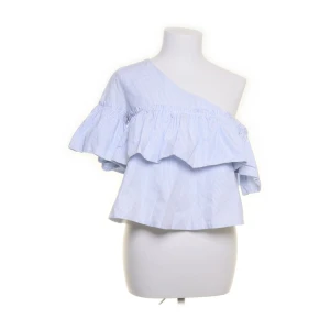 Randig offshoulder topp från Zara - Säljer en ljusblå och vit randig offshoulder topp från Zara Trafaluc Collection. Toppen har volangdetaljer och en ärm, vilket ger en snygg och trendig look. Perfekt för dig som gillar unika snitt och fräscha färger.