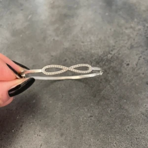 Silverfärgat armband med infinity-symbol - Snyggt armband i silverfärg med en glittrig infinity-symbol framtill. Armbandet är smalt och har en stilren design som passar perfekt för dig som gillar minimalistiska smycken med en liten twist. Perfekt att matcha med andra silversmycken för en cool look.