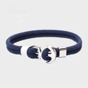 Marinblå armband med ankardetalj - Snyggt marinblått armband med repstruktur och en cool silverfärgad ankare som lås. Armbandet har vita detaljer och passar perfekt för dig som gillar nautisk stil. Materialet är syntet och metallen ger en modern touch.