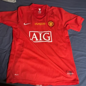Manchester United Ronaldo 7 Finaltröja - Manchester Uniteds officiella matchtröja från Champions League-finalen 2008 med Ronaldo 7 på ryggen. Röd med vita och gula detaljer, AIG-logga på bröstet och broderat klubbmärke. Tillverkad i lätt, ventilerande NikeFIT-material. Perfekt för dig som älskar fotboll och United.