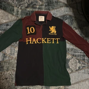 Hackett  pikétröja i blockfärger - Säljer en klassisk pikétröja från Hackett med blockfärger i vinrött, mörkgrönt och marinblått. Original pris 1000kr. Stora broderade detaljer med lejon, siffran 10 och HACKETT-logga framtill. Långärmad och tillverkad i 100% bomull. Perfekt för dig som gillar sportig och preppy stil. passar både S och XS