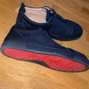 Mörkblå Christian Louboutin sneakers - Snygga mörkblå sneakers från Christian Louboutin i mjuk mocka med klassisk röd sula och rund tå. Skorna har snörning och diskreta detaljer, samt ljusbeige innersida. Perfekt för dig som vill sticka ut med exklusiv stil.