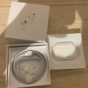 AirPods Pro 2 - Säljer ett par AirPods Pro 2 i mycket fint skick, komplett med originalkartong, USB-C laddkabel och extra öronkuddar. Laddningsfodralet har inga synliga repor eller skador och fungerar perfekt. Perfekt för dig som vill ha aktiv brusreducering och hög ljudkvalitet.