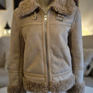 Beige jacka * stl M * piléfodrad - Beige piléfodrad jacka med rejäl dragkedja och möjlighet att spänna kragen högt runt halsen.  * Nypris: 999 kr  * Hela jackan är piléfodrad. Samma material som runt ärmslut, krage etc. * Storlek M. Passar mig som bär 38-40.  * Två sidofickor och två innerfickor.  * Mycket bra skick. Hittar inga fel. * Bröst: ca 53 cm mätt armhåla till armhåla * Höftmått: ca 57 cm. * Axel till ryggslut: ca 60 cm * Innerärm: ca 42 cm.  Djur och rökfritt hem. Se bilder och förstora då de ingår i beskrivningen. Se g