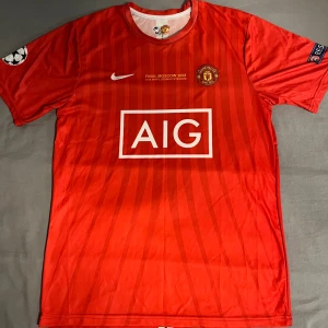 Manchester United Ronaldo 7 Finaltröja - Säljer en röd Manchester United fotbollströja från Champions League-finalen 2008 med Ronaldo 7 på ryggen. Tröjan har vita detaljer, AIG sponsortryck, klubbmärke och Champions League-patch på ärmen. Tillverkad i lätt polyester med subtila ränder och korta ärmar.
