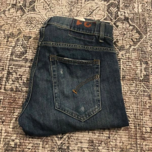 Blå dondup jeans, stl 31 - Säljer ett par snygga blå dondup jeans i storlek 31. Klassisk femficksmodell med raka ben och diskreta slitningar på bakfickorna. Jeansen har en mörk tvätt och är tillverkade i mjukt bomullsmaterial med jeanskänsla. Perfekt för dig som gillar stilrena och bekväma jeans.