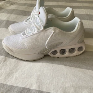 Nike Air Max dn Vita Sneakers - Alldrig använda Nike Air Max Plus sneakers i helvitt med mesh- och syntetmaterial, ikonisk synlig Air Max-dämpning i sulan och diskreta röda detaljer. Skorna har snörning, rund tå och en chunky sula med tydlig struktur undertill. Perfekta för dig som gillar sportig och clean stil.