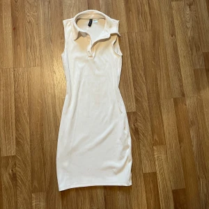 Vit ribbad ärmlös klänning H&M - Snygg vit ärmlös klänning från H&M med krage och knappar framtill. Klänningen är ribbad och har en tight passform som framhäver figuren.