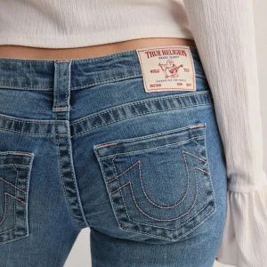 Blå bootcut jeans från True Religion - Snygga blå jeans från True Religion med klassisk bootcut-passform och låg midja. Jeansen har ikoniska bakfickor med kontrastsömmar och patch med logga bak i midjan. Tillverkade i mjukt denim-material med lätt tvättad look. Köpt för 1 400kr, säljer då de är lite för stora för mig. Använda ca 2-3 gånger 