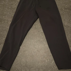 Svarta mjukisbyxor med snörning - Svarta mjukisbyxor med skön passform och snörning i midjan. Perfekta för chill dagar eller träning. Materialet är mjukt och bekvämt, och byxorna har en enkel, stilren look utan mönster eller extra detaljer.