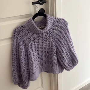 Ljuslila stickad tröja Gina Tricot - Supermysig ljuslila stickad tröja från Gina Tricot med grov ribbad struktur och polokrage. Tröjan är croppad och har långärmade, lite puffiga ärmar som ger en cool och trendig look. Perfekt för att addera färg till din höst- eller vintergarderob.