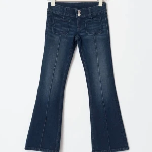 Mörkblå bootcut jeans med fickor - Snygga mörkblå jeans med bootcut passform och framfickor. Jeansen har markerade sömmar längs benen och dubbla knappar i midjan. Perfekt för dig som gillar retrovibbar och vill ha en cool siluett.