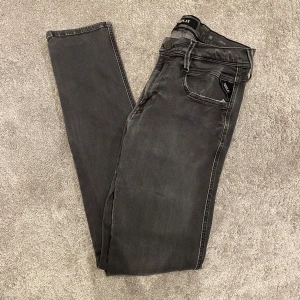 Replay Anbass Jeans - Svarta Replay Hyperflex jeans med skinny passform och klassisk femficksdesign. Jeansen har en lätt tvättad look, dragkedjegylf och stretchigt material för extra komfort. Snygga detaljer på bakfickan och diskret Replay-logga vid fickan.