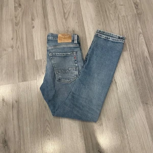 Replay ljusblå raka jeans - Säljer ett par ljusblå jeans från Replay med klassisk femficksdesign och raka ben. Jeansen har slitna detaljer och Replay-logga på bakfickan samt läderpatch i midjan. Perfekta för en avslappnad streetstil.