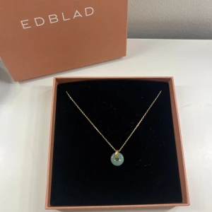 Halsband guld Edblad - Superfint halsband från märket Edblad. Det är guldfärgat och hänget är en grön rund kristall. I nyskick. Asken på bilden följer med vid köp😊