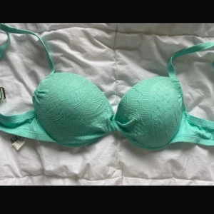 Turkos bikini med snörning och mönster - Säljer en turkos bikini med vadderad bygel-bh och matchande trosa. Båda delarna har ett snyggt strukturerat mönster och trosan har snörning i sidorna med guldiga detaljer. Köpt från secondhand men inte inte använt eftersom de passar inte mig.  Bhn: storlek 38 , trosorna storlek 40 men kan justera banden om man vill ha mindre eller större.