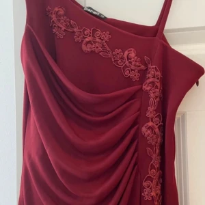 Vinröd långklänning med broderi - Vinröd långklänning med tunna axelband och draperad framsida. Klänningen har vackra blombroderier längs ena sidan och en slits nedtill. Perfekt för dig som vill sticka ut med en elegant och unik look.använd 1 gång. Mycket bra skick. Passar storlek 36-38 är stretch i material.Säljer många fina festklänningar skicka pm.hämtas i norsborg botkyrka.