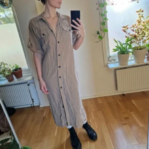 Midi skjortklänning - Lång, beige/ljusbrun/kamelfärgad skjortklänning med korta ärmar och knappar hela vägen framtill. Skulle säga att den är mellan medi/maxi. Skönt tyg med en go buttery-feeling 😍 den har varit i en låda ett litet tag, därav väldigt skrynklig. Blir slät när den är upphängd dock ☺️ Återuppladdad för fri frakt. Jag har mycket annat uppe på sidan, både herr och damkläder. Köp gärna bundle för att få rabatt 🤗 