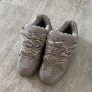 Grå chunky sneakers storlek 44 - Chunky grå sneakers med breda snören och robust sula. Skorna har en blandning av textil och syntetmaterial, med rund tå och platt sula. Perfekta för dig som gillar streetwear och vill ha en clean look med extra volym på fötterna.