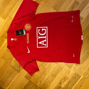 Manchester United Final Moscow 2008 tröja - Säljer en röd Manchester United fotbollströja från Nike, Final Moscow 2008 edition med AIG sponsortryck, broderat klubbmärke och Champions League-märke på ärmen. Ronaldo 7 på ryggen. Tillverkad i lätt och ventilerande material.