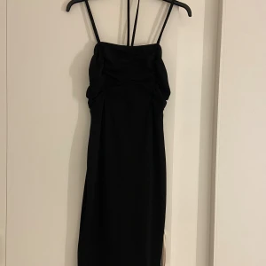 Klänning - Supersnygg svart långklänning från märket WalG, köpt från Zalando. Klänningen har smala axelband, och ett band imitten. Det finns rynkade detaljer upptill. Klänningen har en slits bakom som ger en extra touch och är perfekt för dig som gillar stilrena och trendiga plagg. Matrialet är jättebra, använd en gång innan, med andra ord helt ny. 